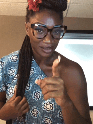 a woman wearing glasses and a flower in her hair is giving a thumbs up