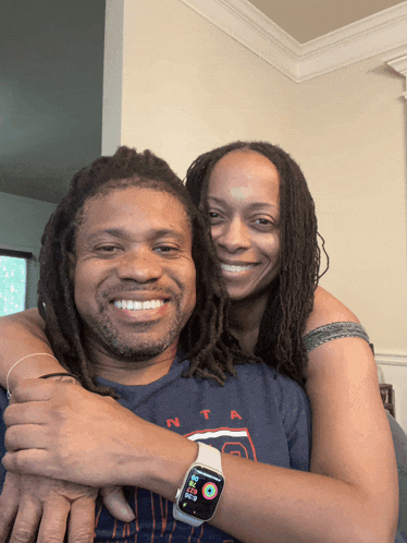 a man wearing an apple watch is hugging a woman wearing a shirt that says nta