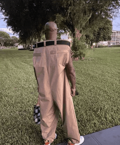 a man wearing a jumpsuit with a belt around his waist is standing in a park