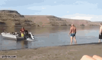 a group of people are standing on a beach next to a boat that is going down the water .