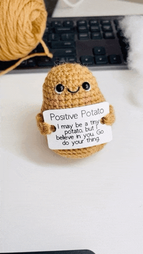 a crocheted potato holds a sign that says positive potato