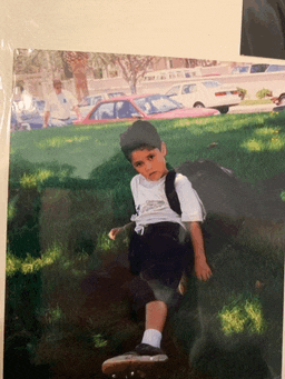 a young boy with a backpack sits on a skateboard in the grass