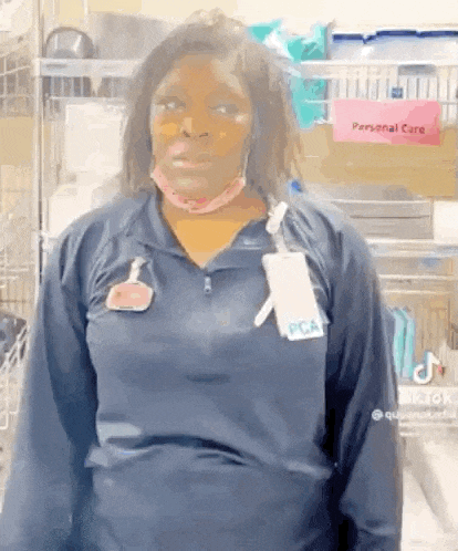 a woman wearing a blue shirt and a name tag is standing in a room with a sign that says personal care .