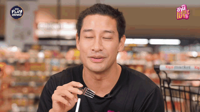 a man in a black shirt is eating with a fork in front of a sign that says play growing