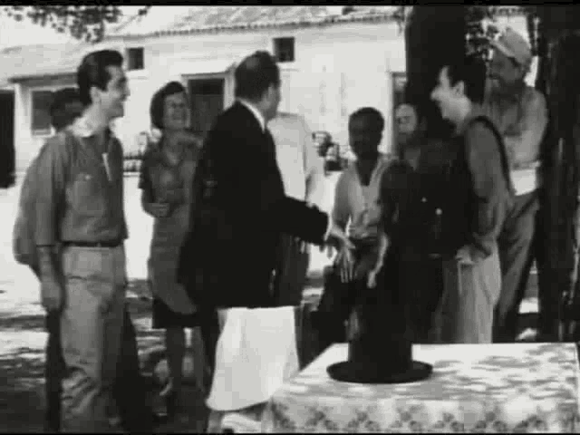 a group of people are standing around a table talking to each other in a black and white photo .