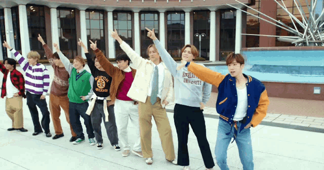 a group of young men are standing in front of a building with one wearing a sweatshirt that says boston college