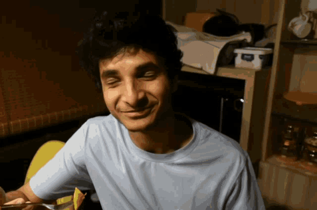 a man in a blue t-shirt is smiling in front of a shelf with a container of yogurt on it