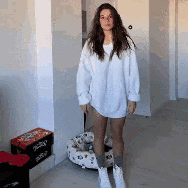 a woman in a white sweater is standing in front of a dog bed with a box that says baby on it