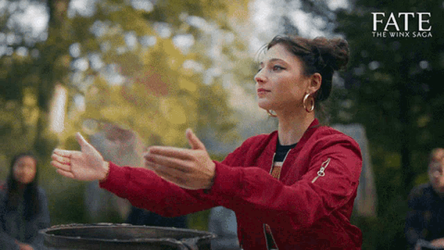 a woman in a red jacket is standing in front of a cauldron with the word fate on the bottom right