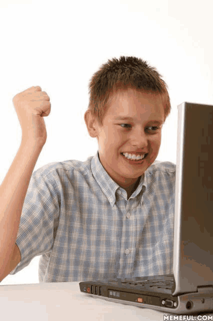 a young boy sitting in front of a laptop with his fist up