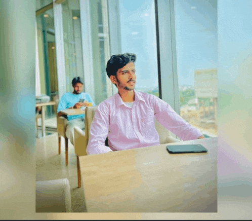 a man in a pink shirt sits at a table with a tablet on it