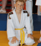 a young boy in a white karate uniform with a yellow belt sits on the floor