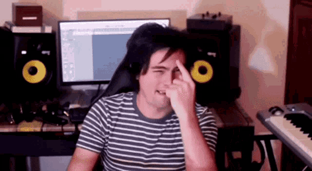 a man in a striped shirt is sitting at a desk in front of a computer and a keyboard .