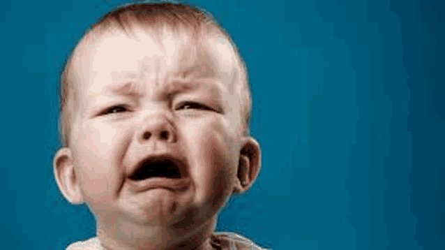 a baby is crying with his mouth open and a blue background .