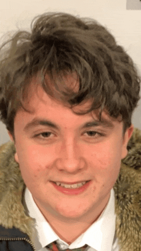 a young man wearing a fur coat and tie smiles