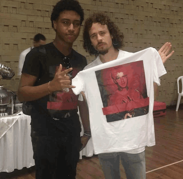 two men standing next to each other one holding a t-shirt with a picture of eminem on it