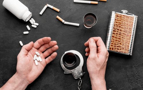 a man in handcuffs is holding a glass of alcohol and a bottle of pills