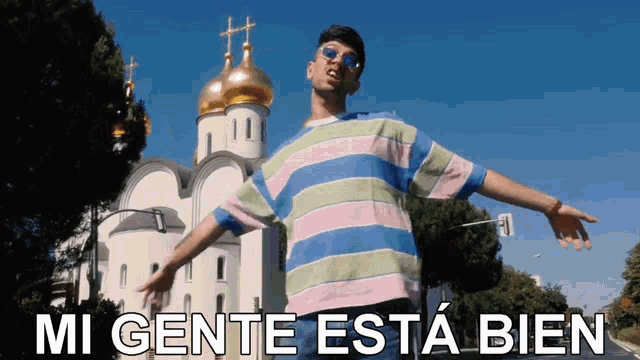 a man in a striped shirt is standing in front of a church with the words " mi gente esta bien " on the bottom