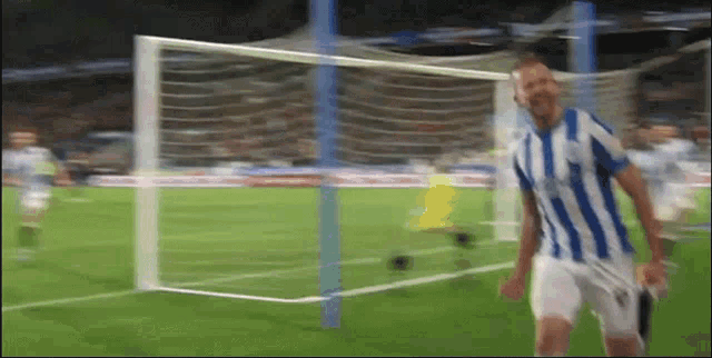 a man in a blue and white striped shirt is standing on a soccer field in front of a goal