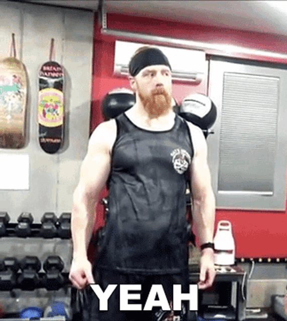 a man with a beard wearing a black tank top is standing in a gym with the word yeah written on the bottom