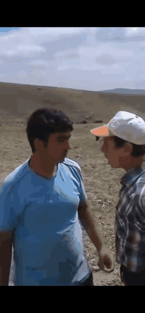 two men are standing next to each other on a dirt road .