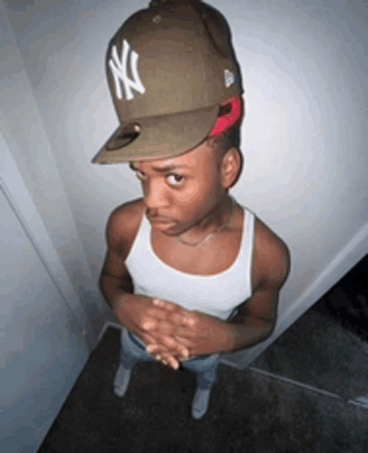 a young man wearing a ny hat and a tank top