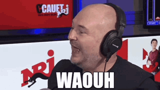 a bald man wearing headphones says waouh in front of a radio station