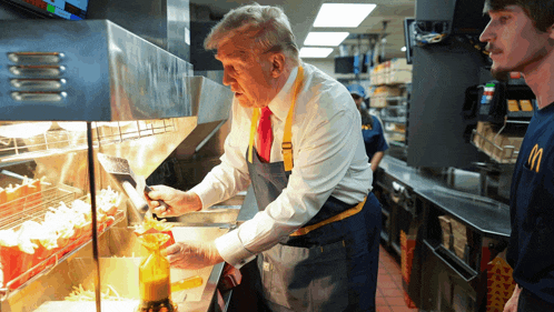 a man in an apron is pouring sauce on french fries in a mcdonald 's kitchen