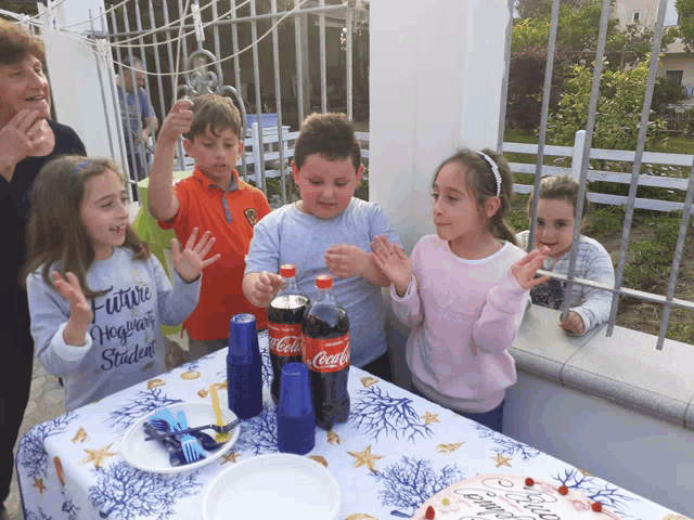 a group of children are standing around a table with a bottle of coca cola on it