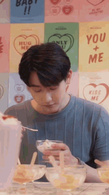 a man eating ice cream in front of a wall with valentine 's day cards on it including one that says hug me