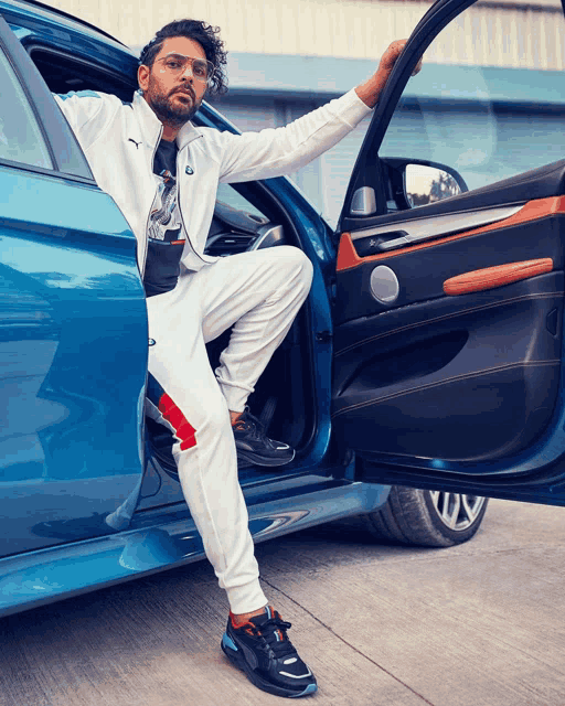 a man in a white puma suit is sitting in a blue bmw