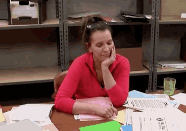 a woman in a red shirt sits at a desk with papers on it and a paper that says blue on it