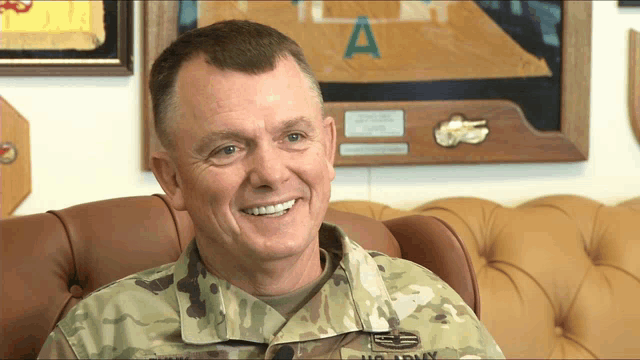 a man in a us army uniform is smiling in front of a plaque that says a