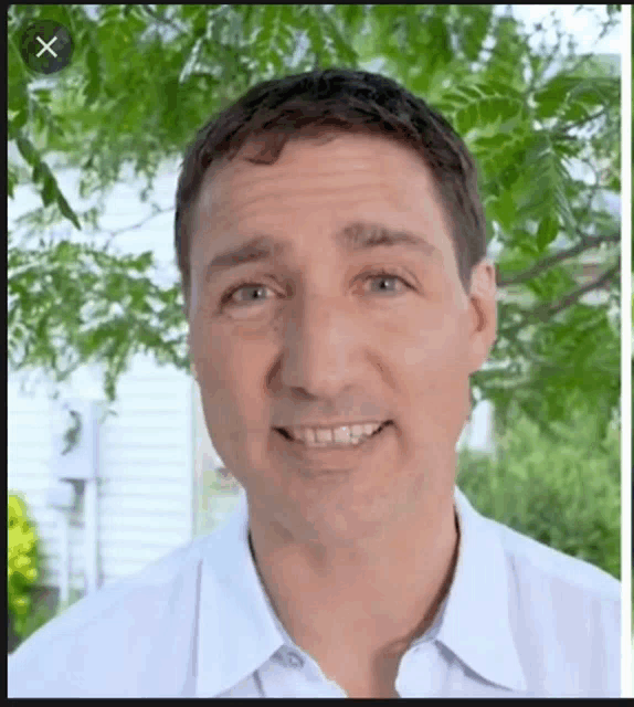 a man in a white shirt is smiling in front of a tree with an x in the corner