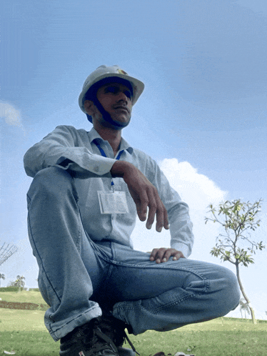 a man wearing a hard hat and a name tag sits in the grass