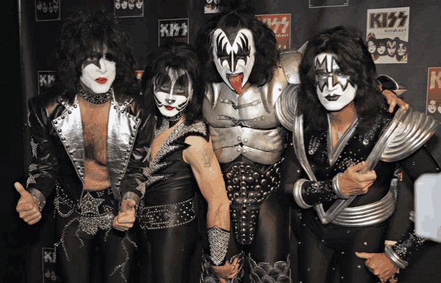 a group of kiss members pose for a photo in front of a kiss poster