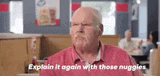 an older man in a red shirt is sitting at a table in a restaurant and talking to someone .