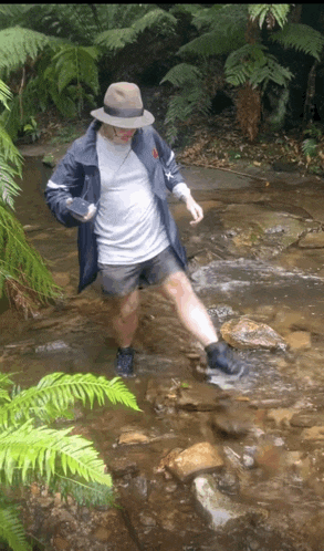 a man wearing a hat and a jacket is crossing a stream