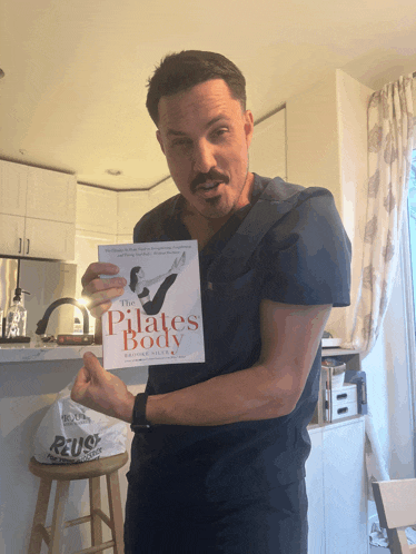 a man in scrubs holds up a book titled the pilates body