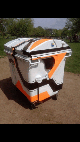 a white trash can with orange and black stripes sits in the dirt