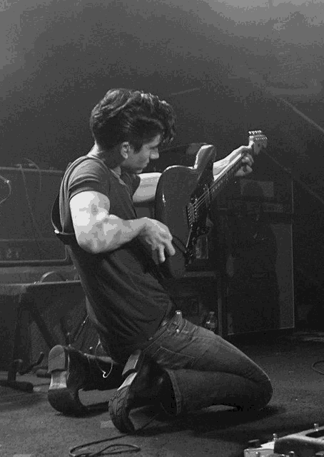 a man is kneeling down while playing a guitar with the letter e on the neck