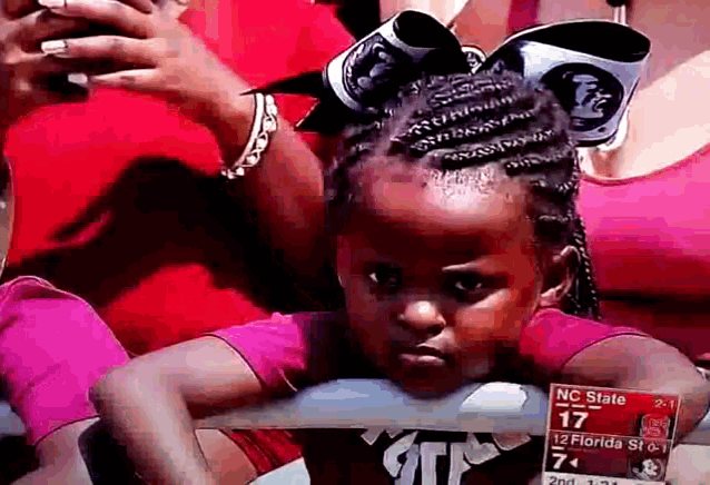 a little girl with a bow in her hair is watching a game between nc state and 12 florida state