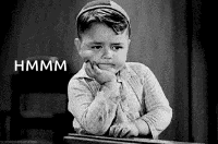 a black and white photo of a young boy sitting at a desk with his hand on his face .