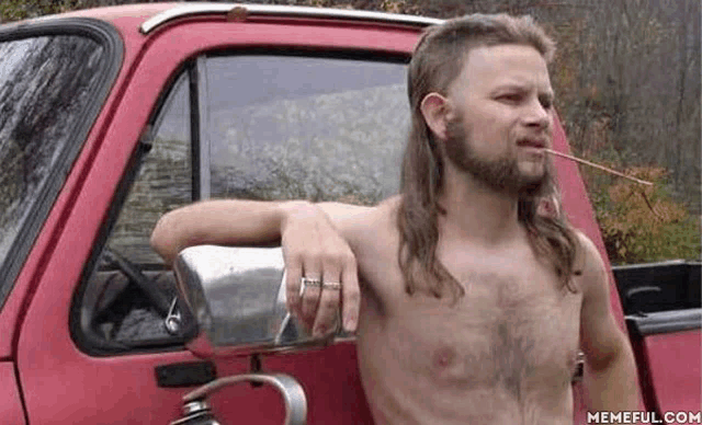 a shirtless man with a mullet and a beard is leaning against a red truck .