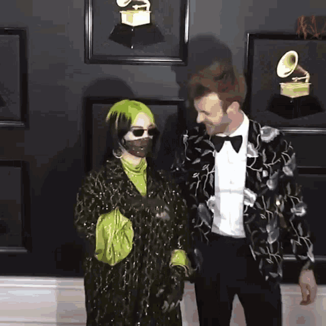 a man and a woman are standing next to each other in front of a wall with grammy trophies on it