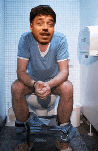 a man in a blue shirt is sitting on a toilet with his pants down