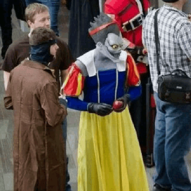 a man in a snow white costume is holding an apple while standing in a crowd .