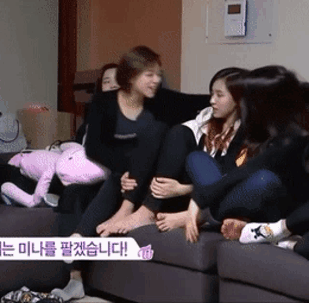 a group of women are sitting on a couch with a pink stuffed animal behind them