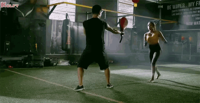 a man and a woman are practicing martial arts in front of a sign that says " be water "