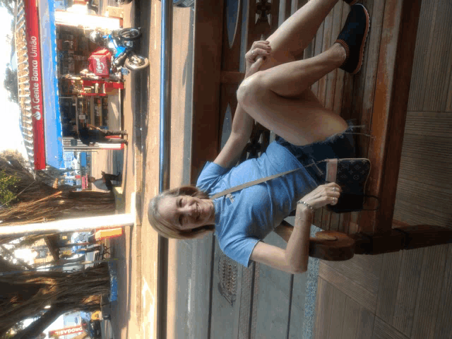 a woman sits on a wooden bench in front of a gas station that says a gente bonita unido